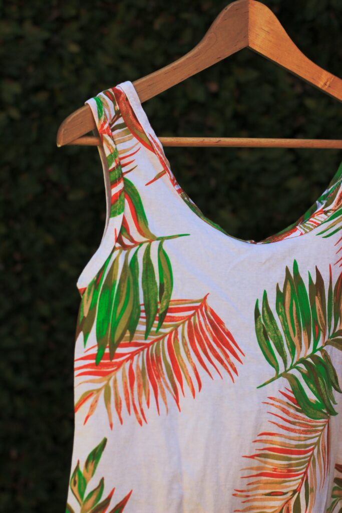 Close-up of a tropical leaf-patterned dress hanging on a wooden hanger.